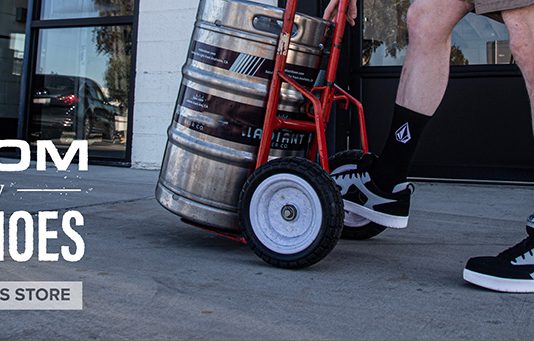 man wearing Volcom work shoes pushing a cart with a barrel