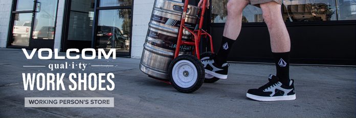 man wearing Volcom work shoes pushing a cart with a barrel